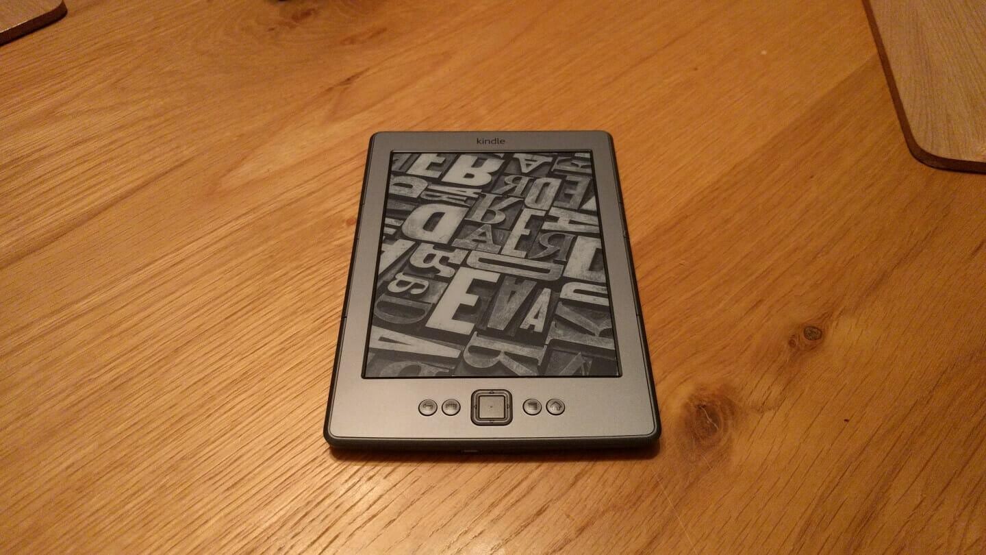 Old Kindle in Screensaver mode on a wooden table