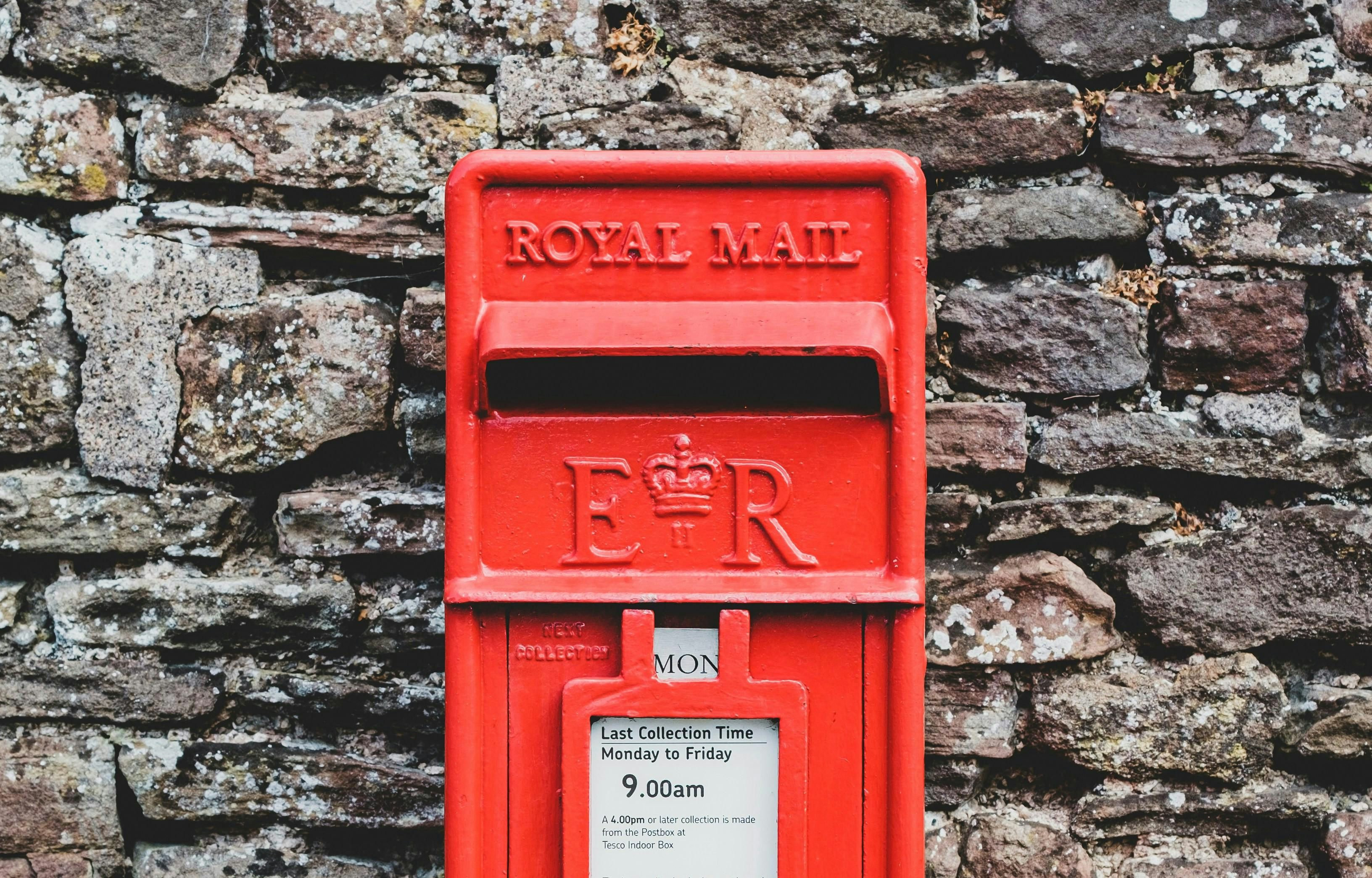 Old School red British post box in front of a brick  wall