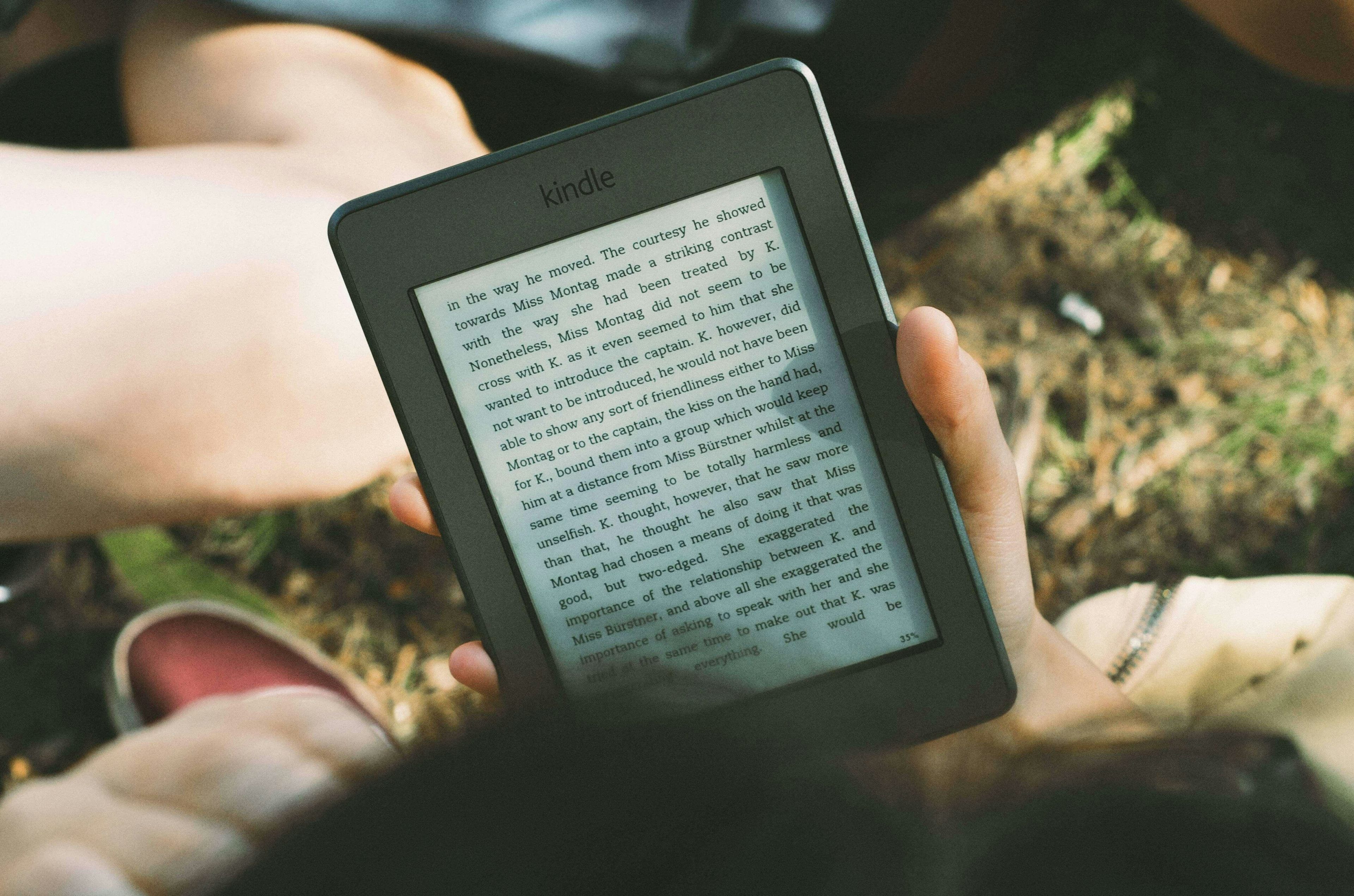 Amazon kindle being held by someone sitting on grass with friends.